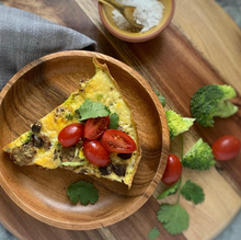 Load image into Gallery viewer, image of quiche with vegetables on a cutting board with broccoli and tomato
